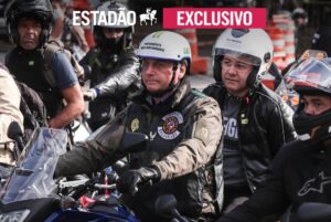 Imagem do ex-presidente Bolsonaro guiando uma moto com homem na garupa durante motociata.