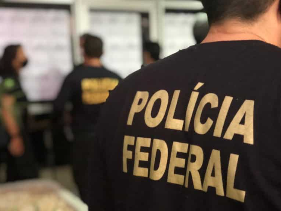 Imagem de policial federal de costas com nome Polícia Federal em primeiro plano.