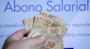 Imagem de uma mão com cédulas de 50 reais e o nome "Abono Salarial" em plano de fundo.