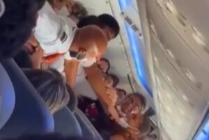 Imagem de confusão entre as mulheres dentro do avião e os comissários tentando apartar.