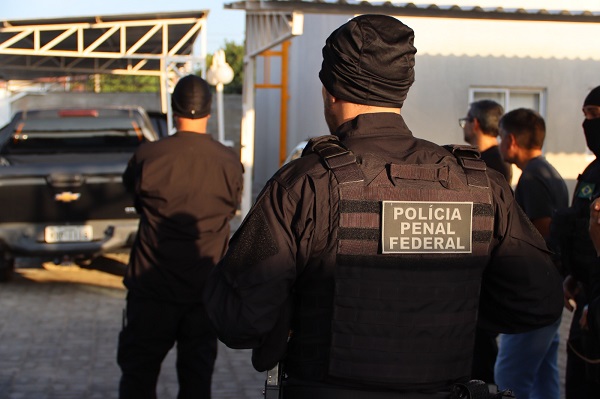 Imagem de agentes das polícias de costas em operação de buscas, prisões e apreensões.